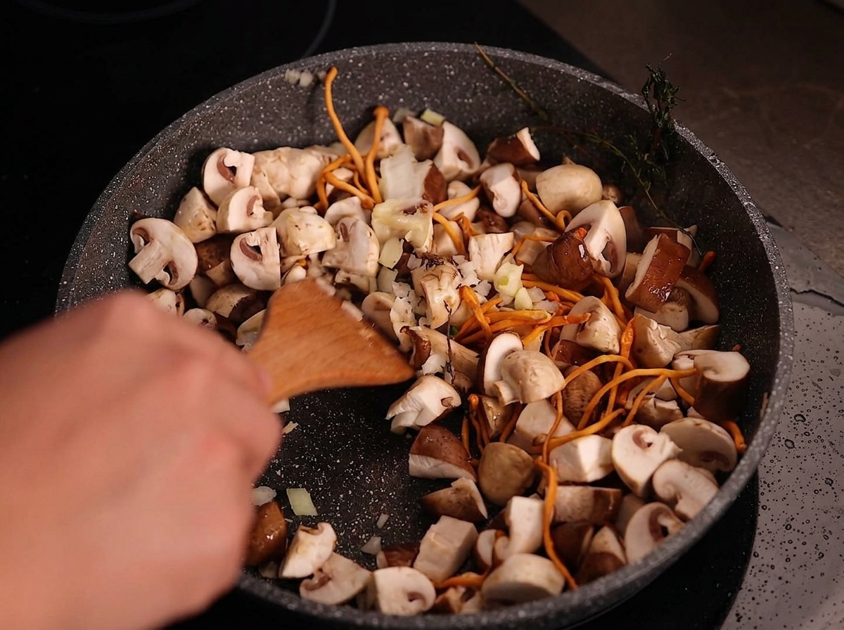 Spatule mélangeant loignon haché et lail émincé avec les champignons cuits.