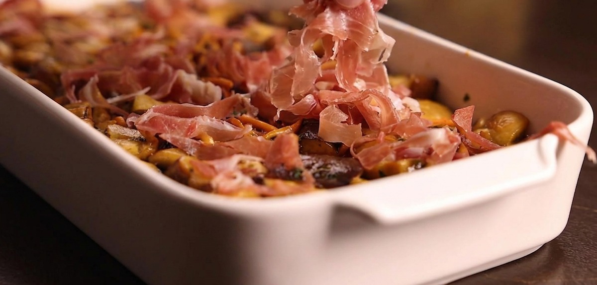 Mains déposant des lanières de jambon cru sur le lit de champignons dans le plat.