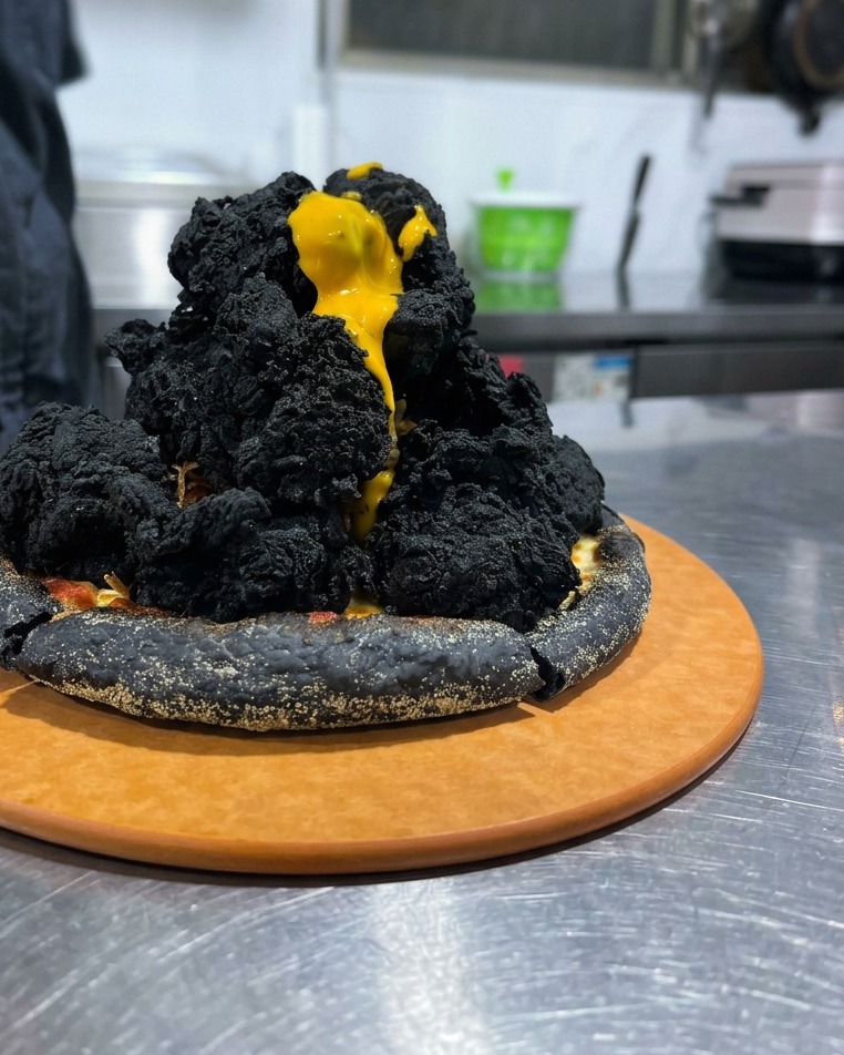 Sauce fromage jaune coulant comme de la lave sur une montagne de poulet noirci posée sur une pizza.
