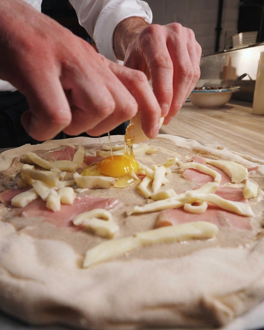 Mains dun chef cassant un œuf frais au centre dune pizza crue.