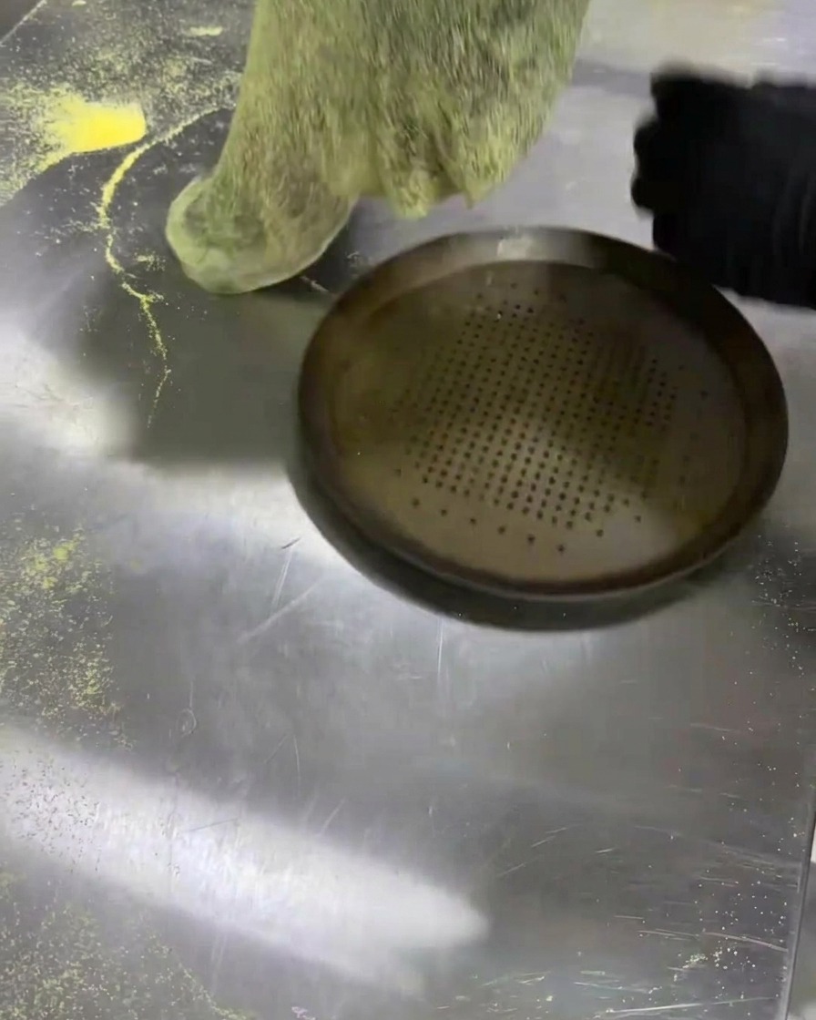 Transfert dun disque de pâte noire sur une plaque à pizza en métal perforée.