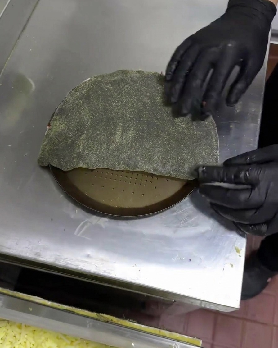 Mains gantées repliant la pâte noire pour former un calzone en forme de demi-lune.