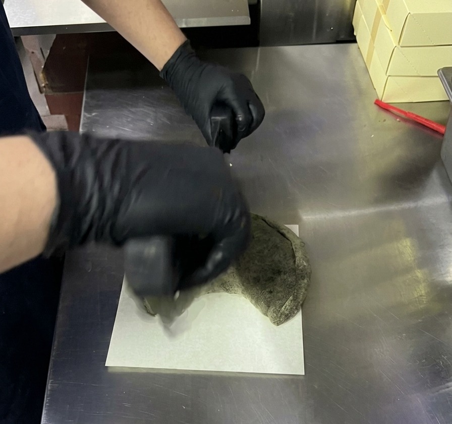Découpe dun calzone noir cuit avec un couteau berceuse à pizza sur une planche blanche.