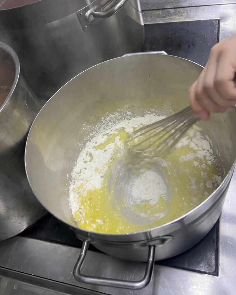 Une main fouettant vigoureusement la farine dans le beurre fondu pour créer un roux dun jaune pâle.