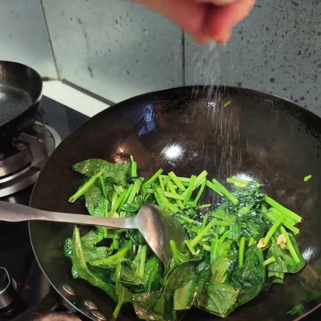 Une main saupoudrant du sel sur les épinards sautés dun vert éclatant dans un wok.