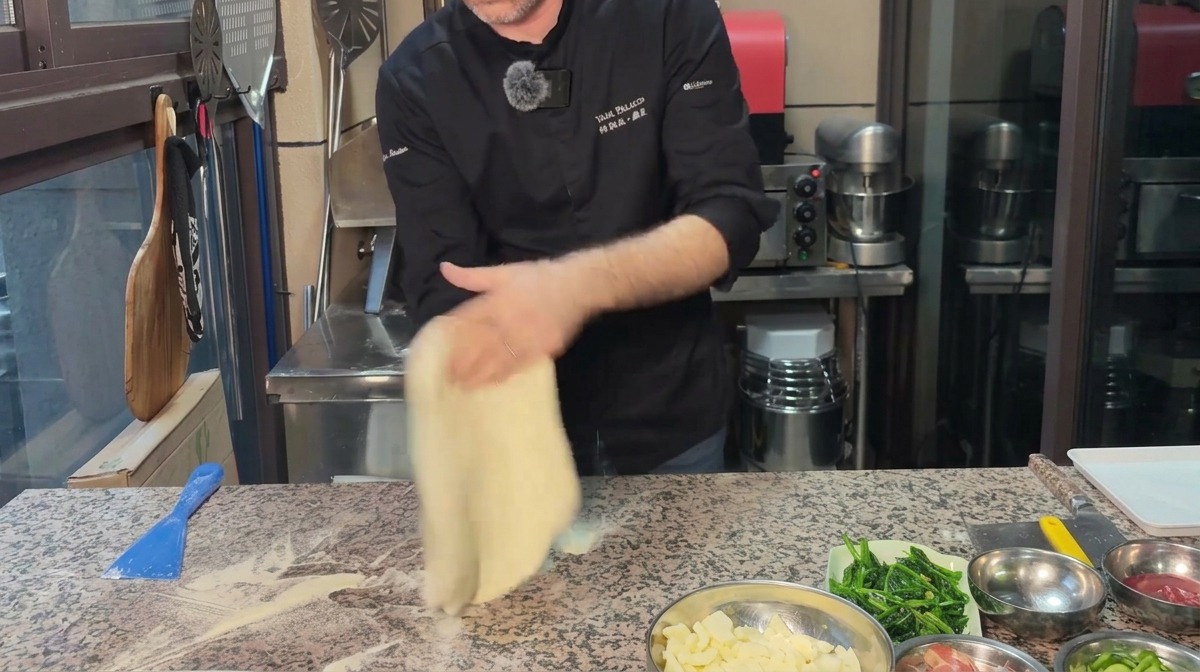 Un chef étirant une pâte à pizza en cercle sur un plan de travail en marbre fariné.