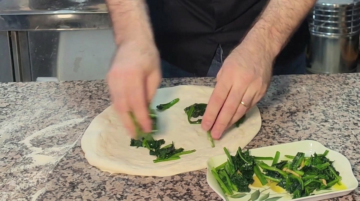 Mains répartissant uniformément les épinards cuits sur la base de pizza crue.