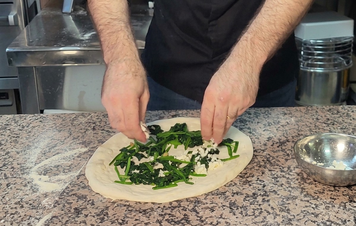 Mains saupoudrant de la feta émiettée sur le lit dépinards de la pizza.