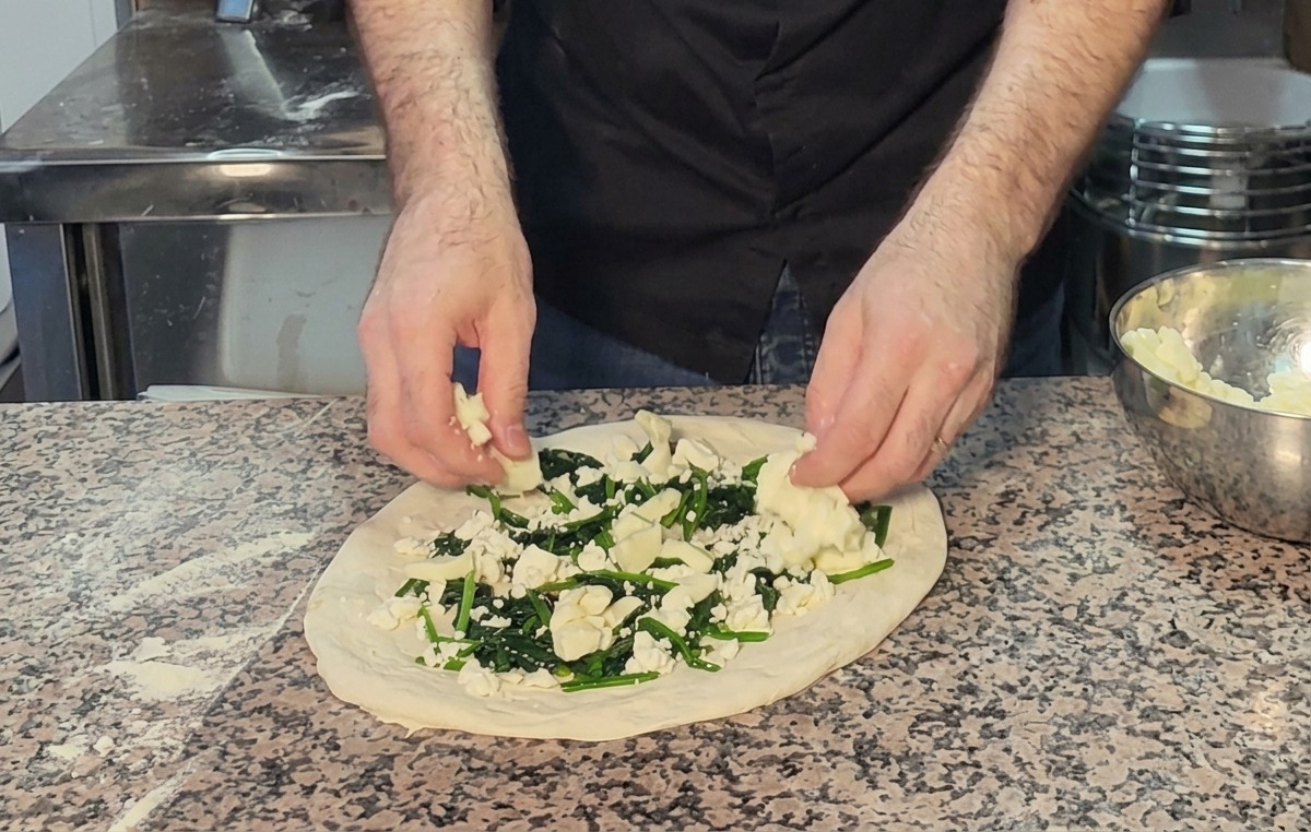 Dépôt de morceaux de mozzarella sur la pizza garnie dépinards et de feta.