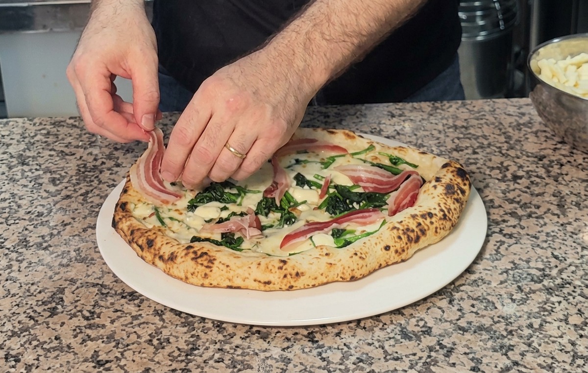 Disposition de fines tranches de pancetta sur la pizza brûlante sortant du four.
