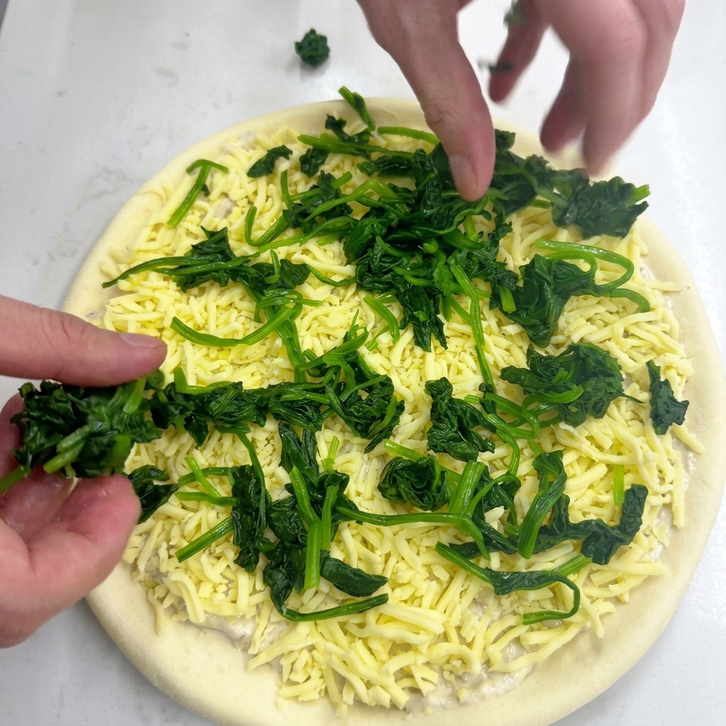 Deux mains disposant des petits tas dépinards verts blanchis sur la mozzarella.