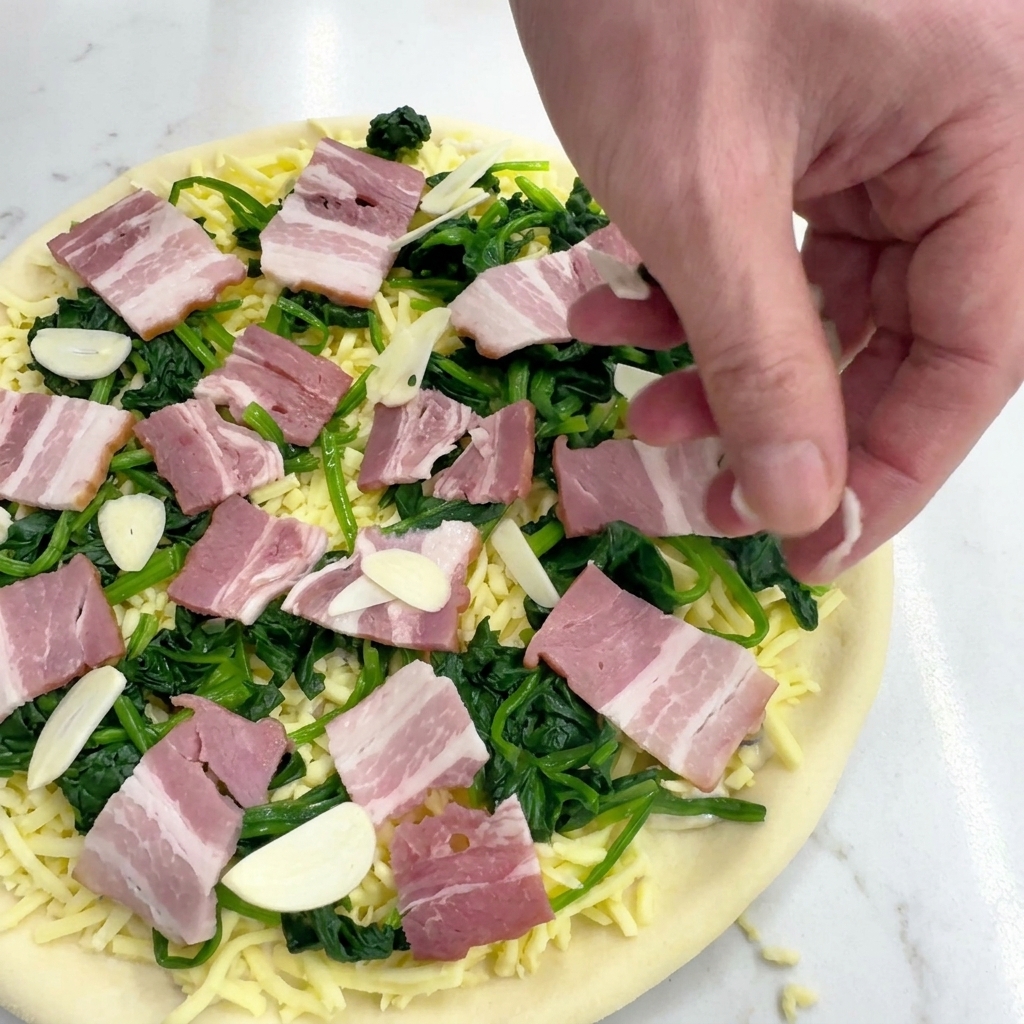 Une main éparpillant de fines tranches dail frais sur la garniture de la pizza.