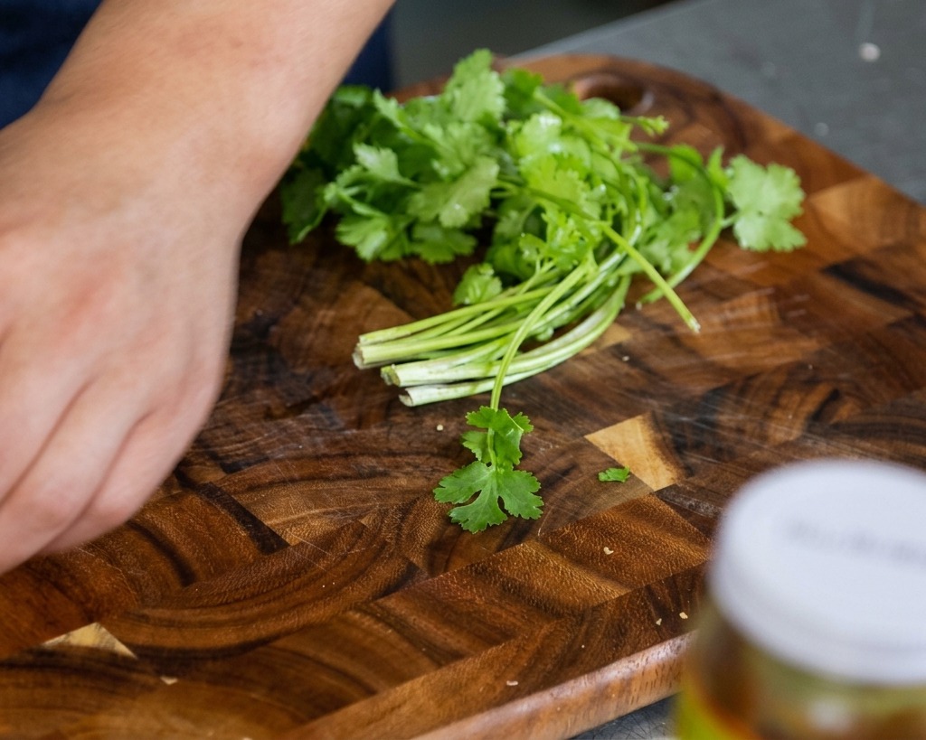 Feuilles et tiges de coriandre fraîche sur une planche en bois, prêtes à être ciselées à la main.