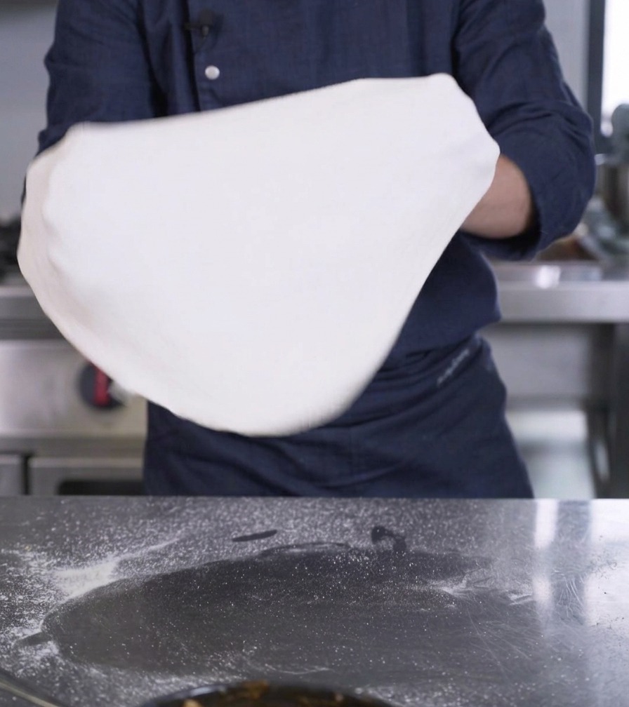 Mains étirant un grand disque de pâte à pizza blanche et fine.