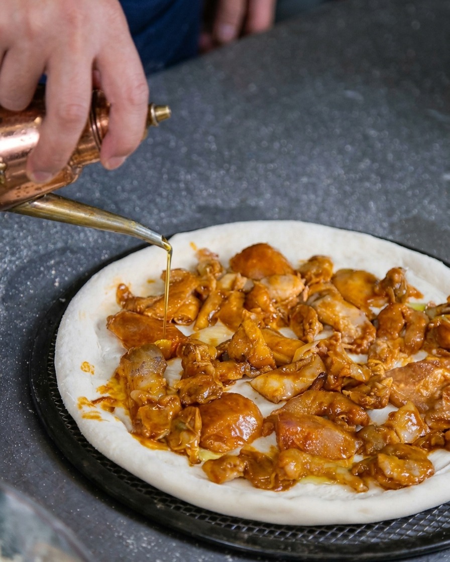 Main utilisant un huilier pour arroser légèrement dhuile dolive une pizza garnie de fruits de mer avant cuisson.