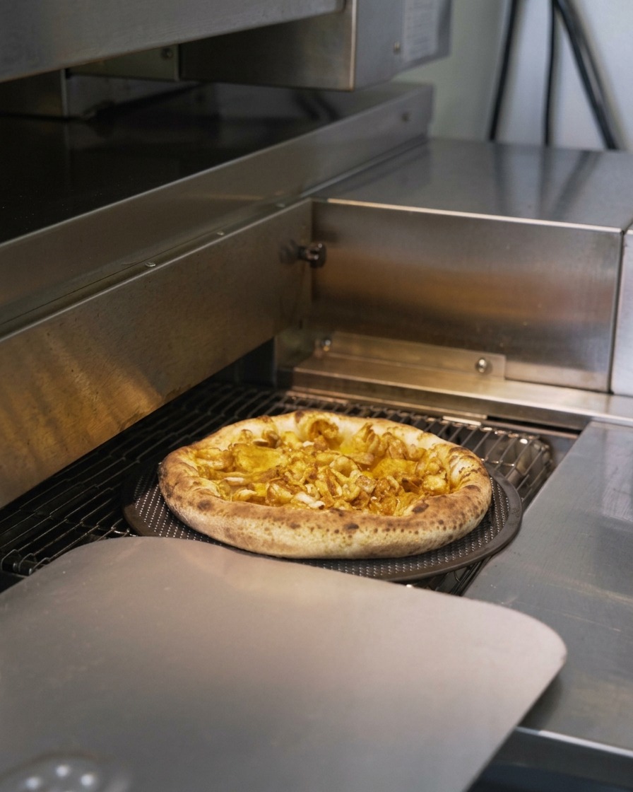 Une pizza aux fruits de mer passant dans un four convoyeur, la croûte gonfle et commence à dorer.