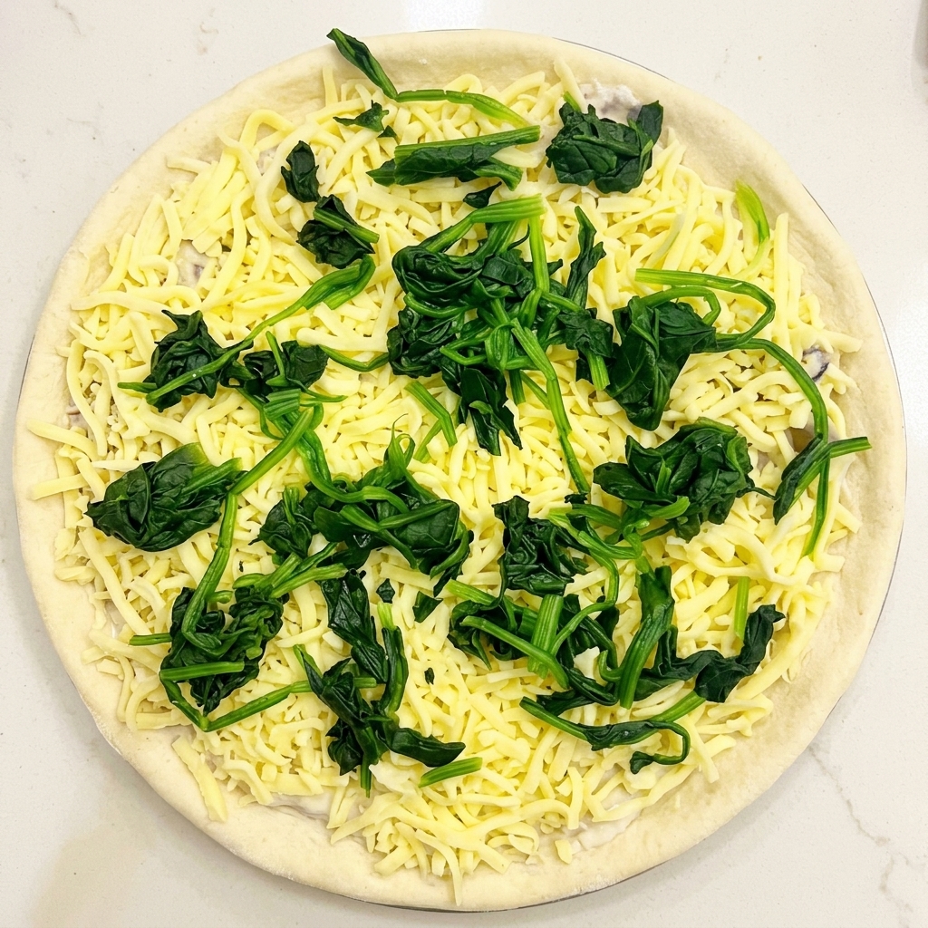 Vue de dessus dune pâte à pizza garnie de sauce, de fromage et de petits tas dépinards blanchis.