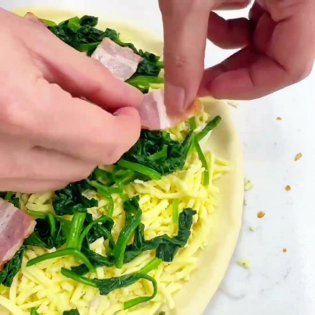 Mains déposant des carrés de bacon cru sur une pizza garnie de fromage et dépinards.