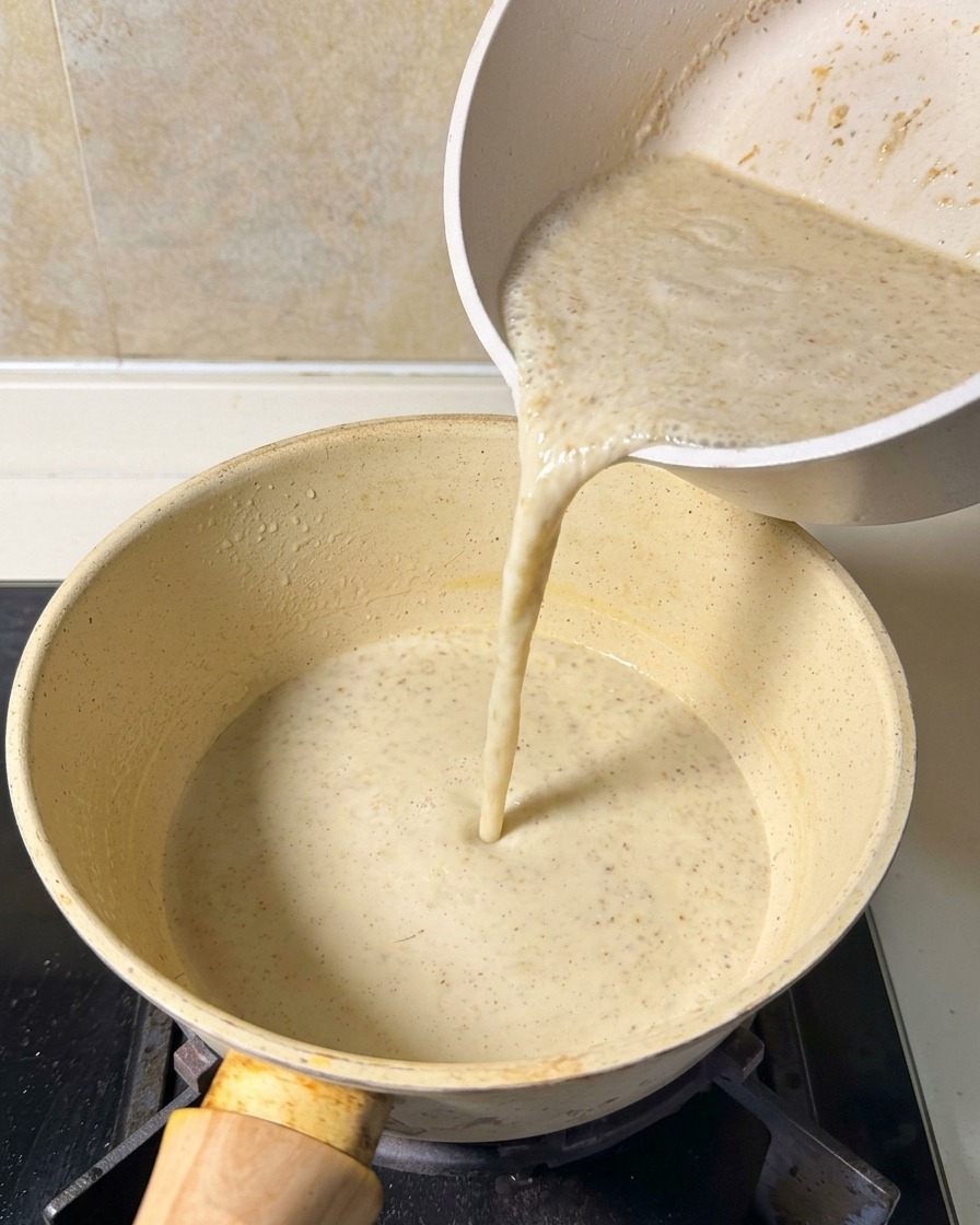 Le mélange de soupe lisse et beige versé dans une casserole sur une cuisinière.