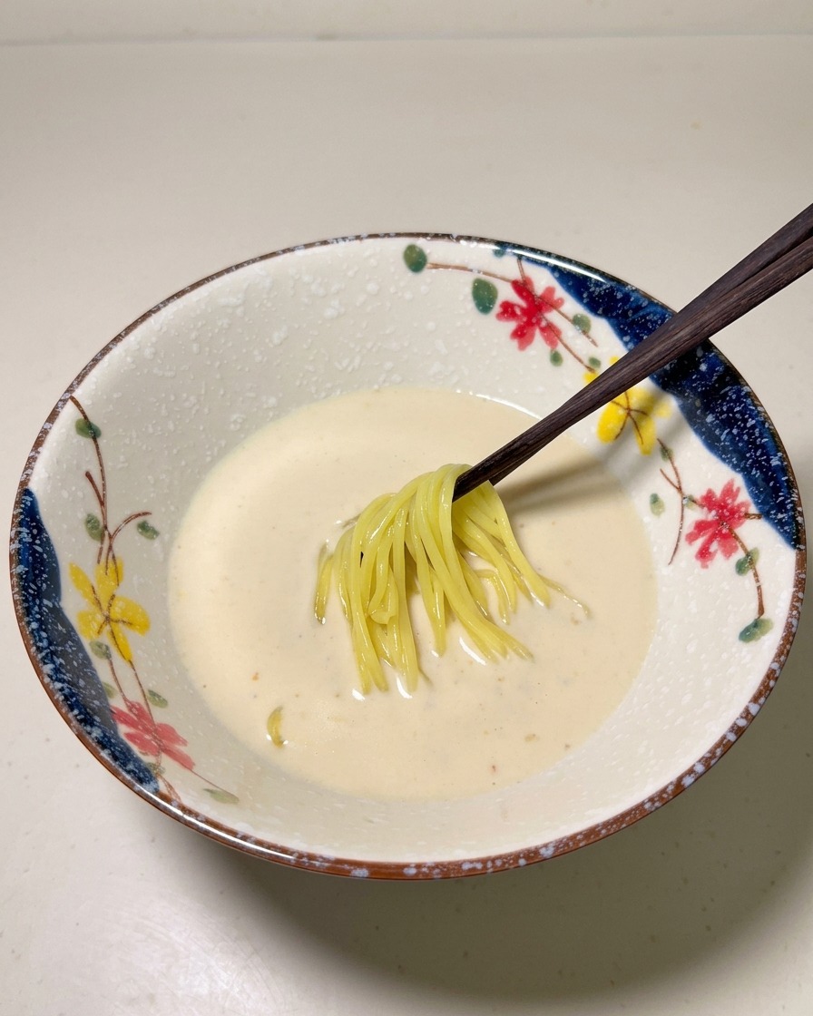 Des nouilles ramen jaunes cuites déposées au centre du bouillon crémeux dans un bol.