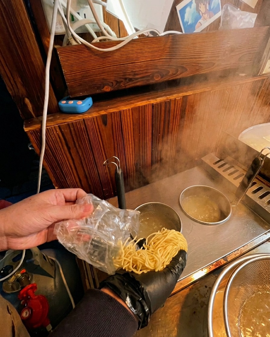 Des nouilles ramen fraîches versées depuis un sachet plastique dans un panier de cuisson immergé dans leau bouillante.