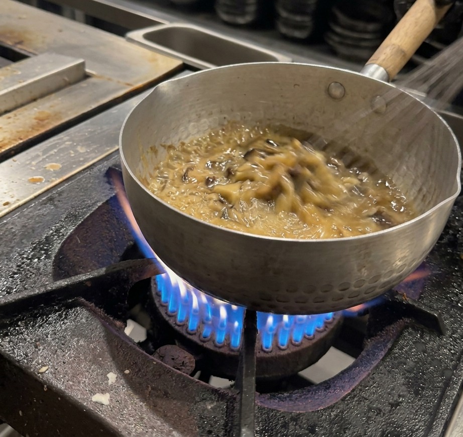 Un fouet mélangeant continuellement une sauce brun foncé épaisse et bouillonnante dans une casserole.