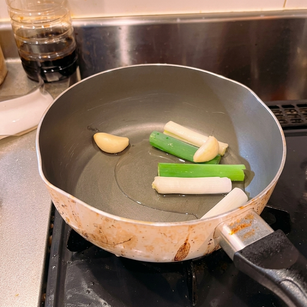 Oignons verts et gousses dail entières reposant dans un fond dhuile froide à lintérieur dune casserole.