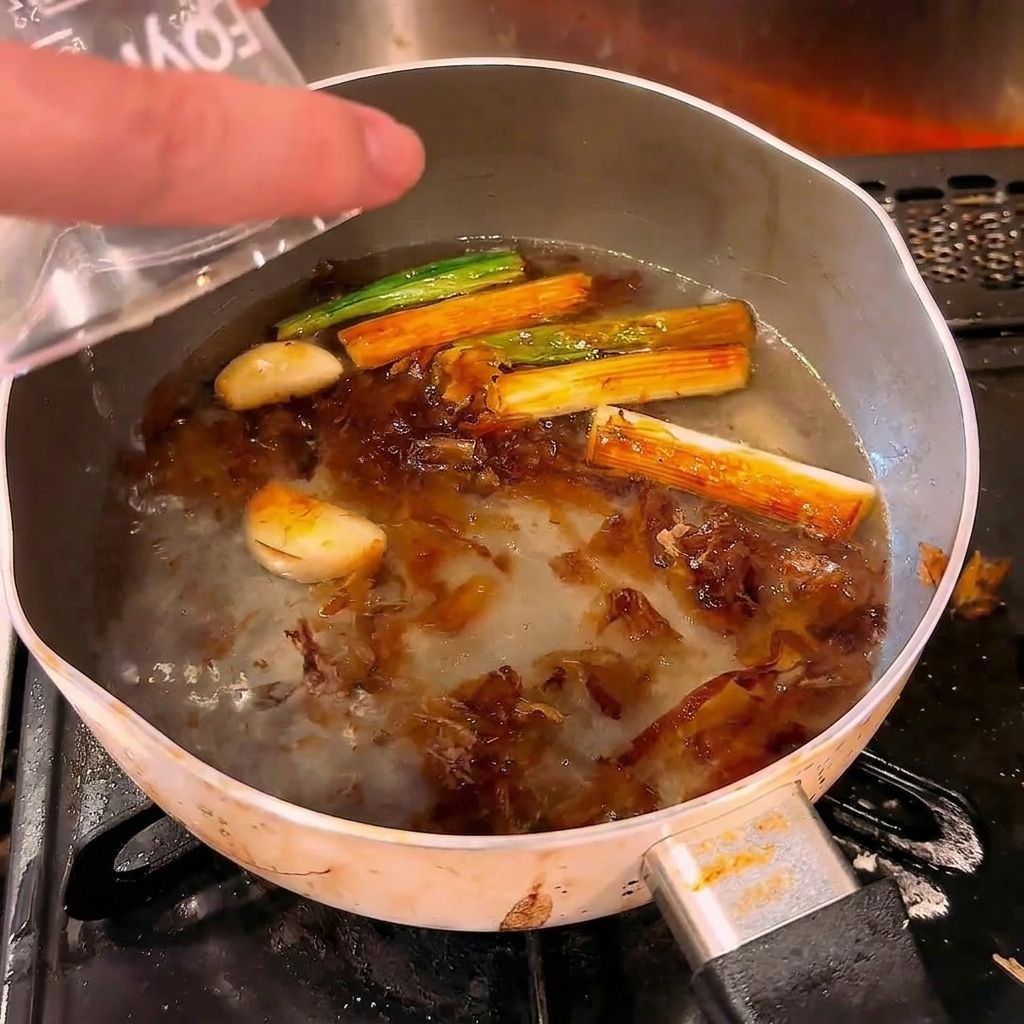 De leau claire versée depuis un verre doseur dans une casserole chaude contenant les aromates rôtis.