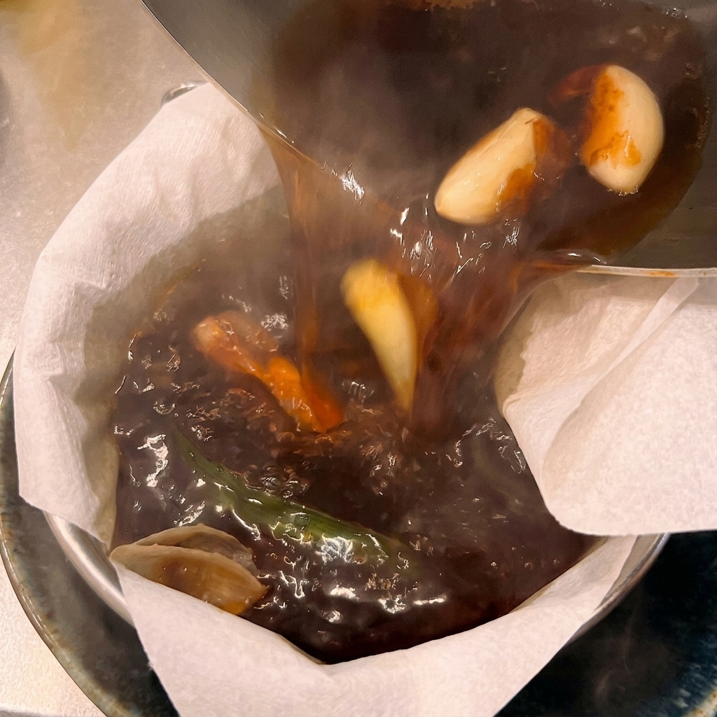 Bouillon de ramen chaud et sombre filtré à travers un filtre en papier blanc au-dessus dun bol de service.