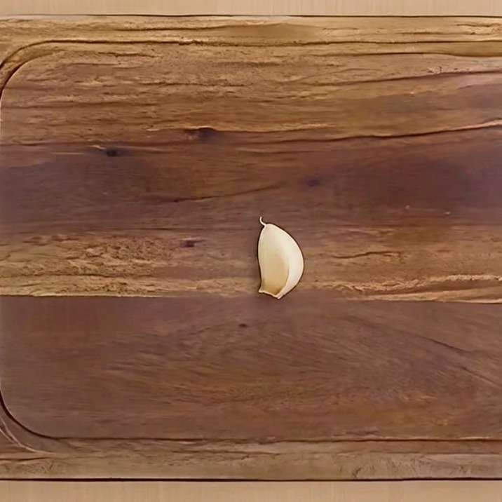 Une gousse dail épluchée, coupée en deux avec le germe retiré, sur une planche à découper en bois.