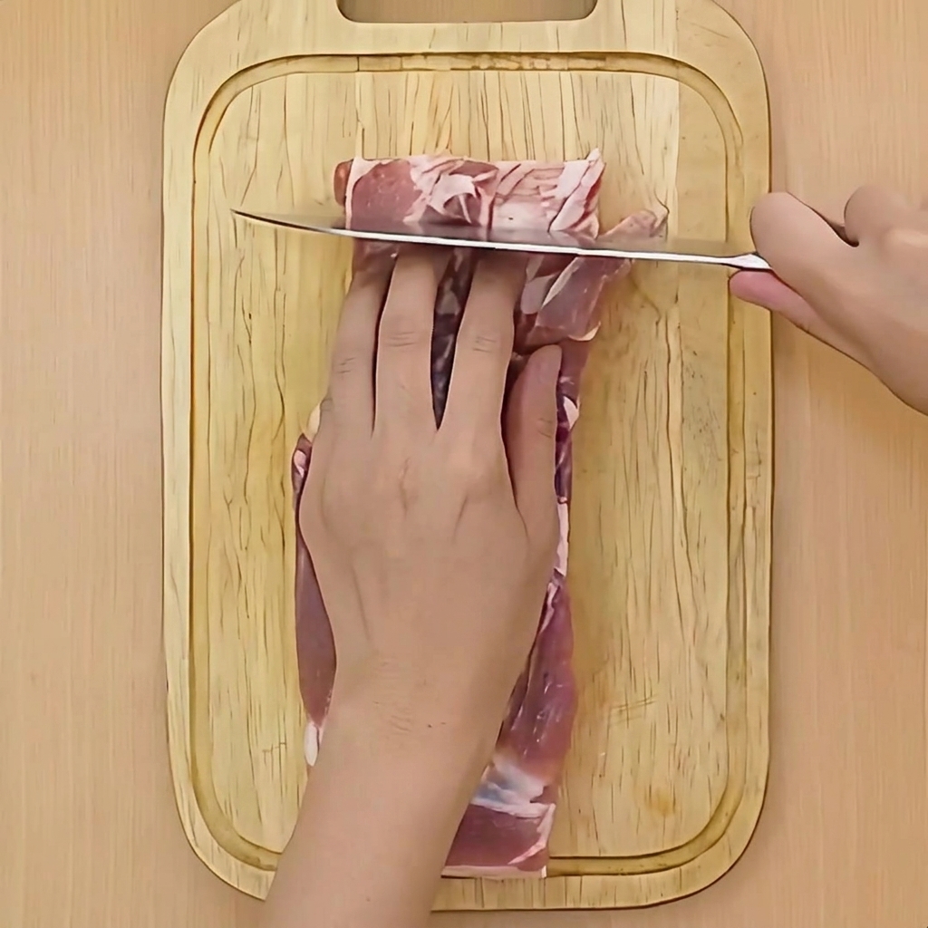 Une main tenant un couteau et pratiquant des incisions horizontales peu profondes dans la poitrine de porc crue.