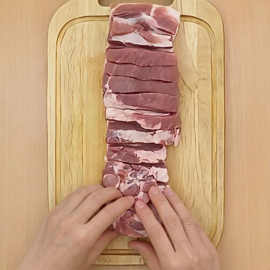 Deux mains roulant fermement un bloc de poitrine de porc crue en forme de cylindre sur une planche.