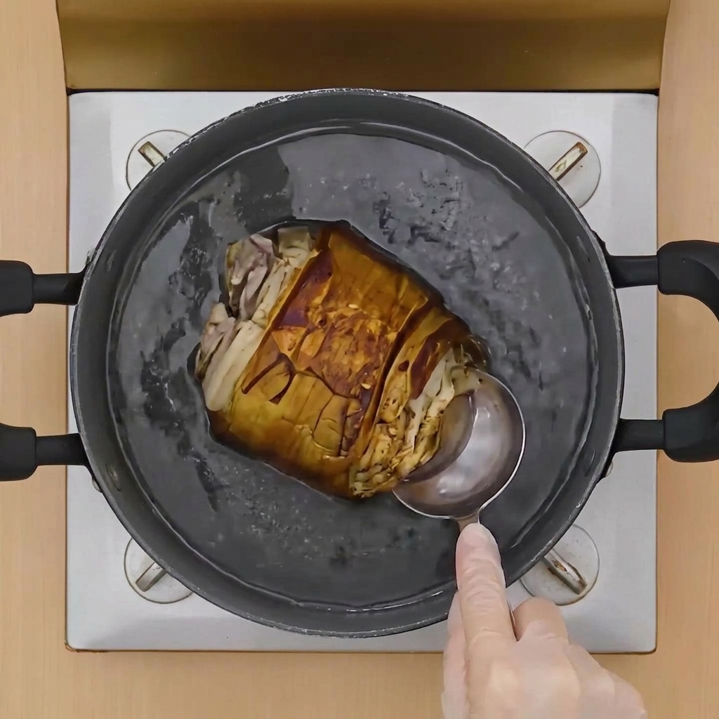 Une louche versant du liquide sur un rouleau de porc doré dans une cocotte de bouillon frémissant.