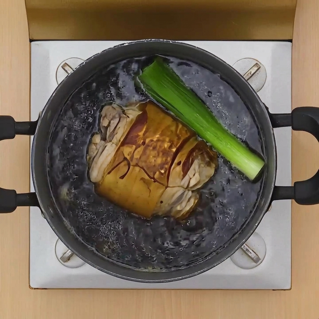 Un rouleau de porc mijotant dans un bouillon sombre aux côtés dun grand morceau doignon vert.