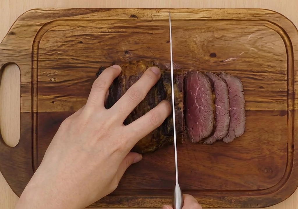 Des mains tenant fermement le porc braisé tout en le découpant en fines rondelles avec un couteau bien aiguisé.