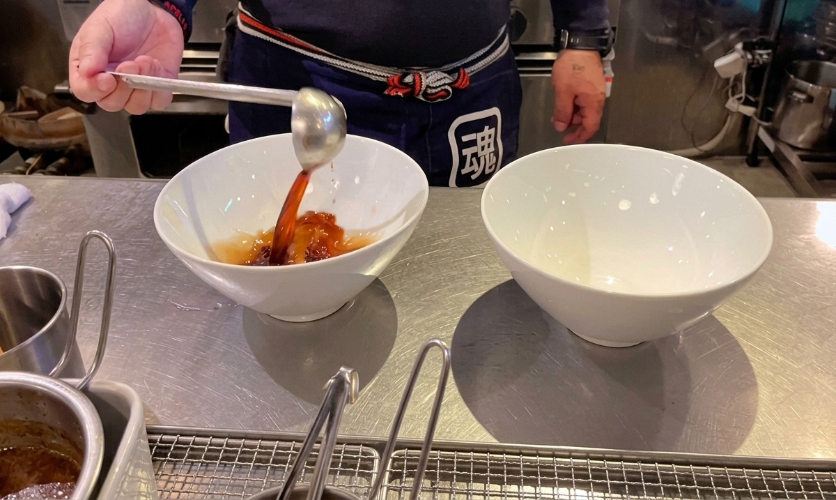 Chef versant le tare de soja sombre dans des bols à ramen blancs.