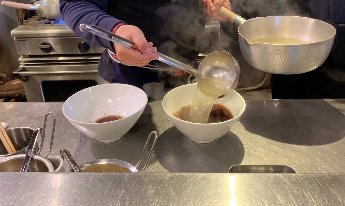 Bouillon clair fumant versé dans les bols sur le tare de soja sombre.