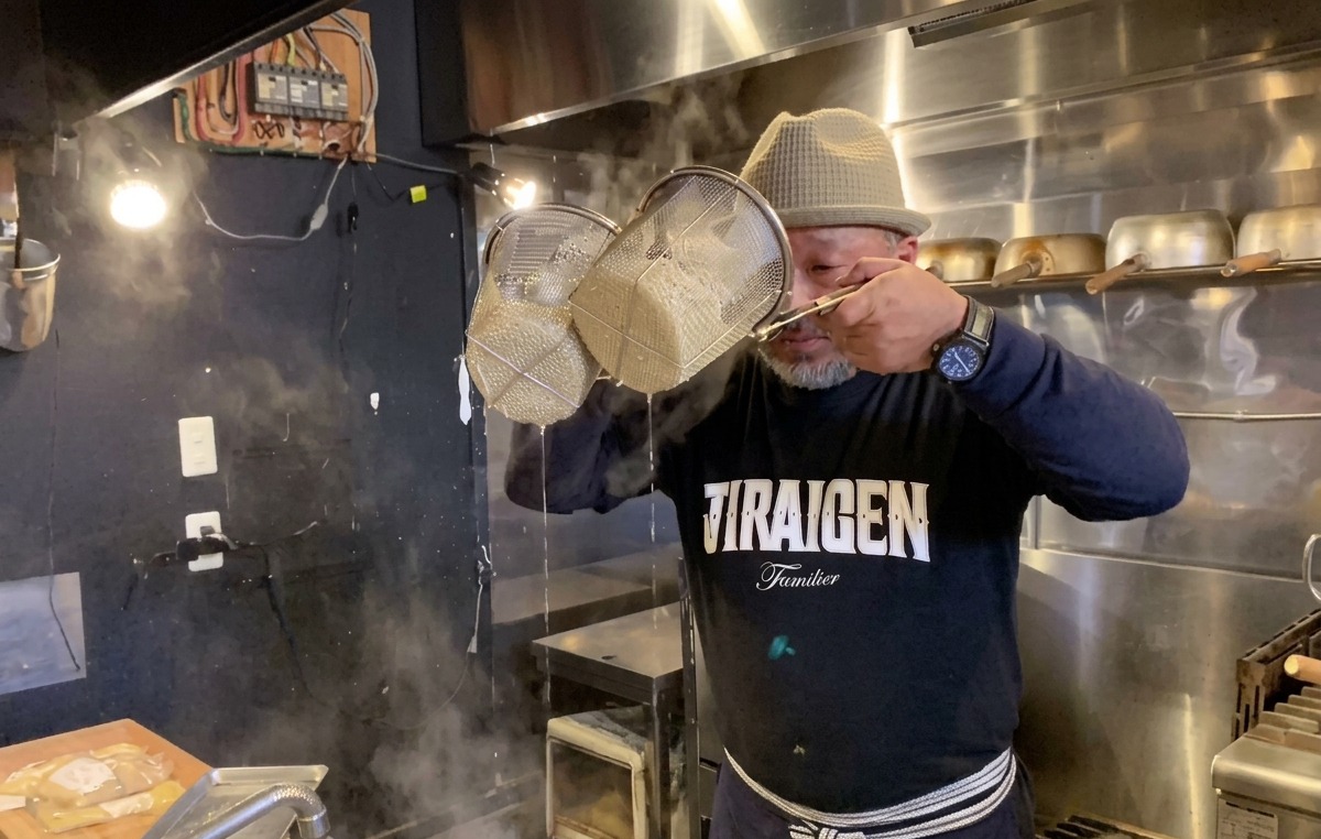 Chef secouant vigoureusement les passoires à nouilles pour en extraire leau de cuisson.