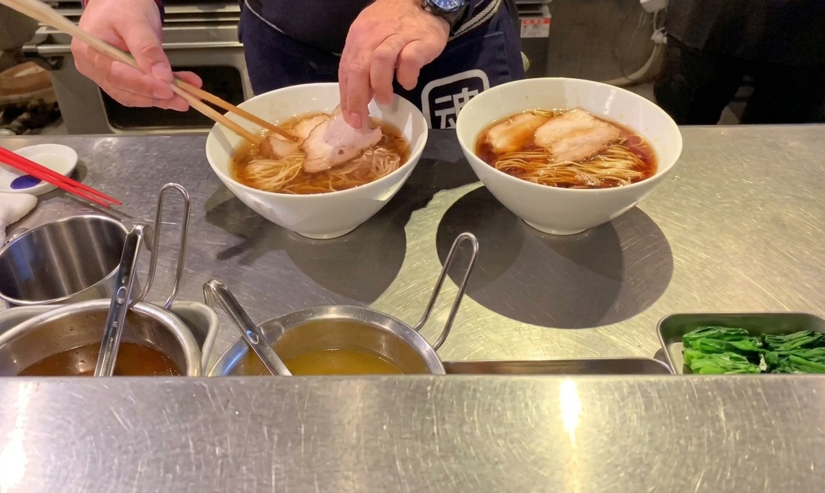 Chef déposant des tranches de porc chashu sur les nouilles à laide de baguettes.
