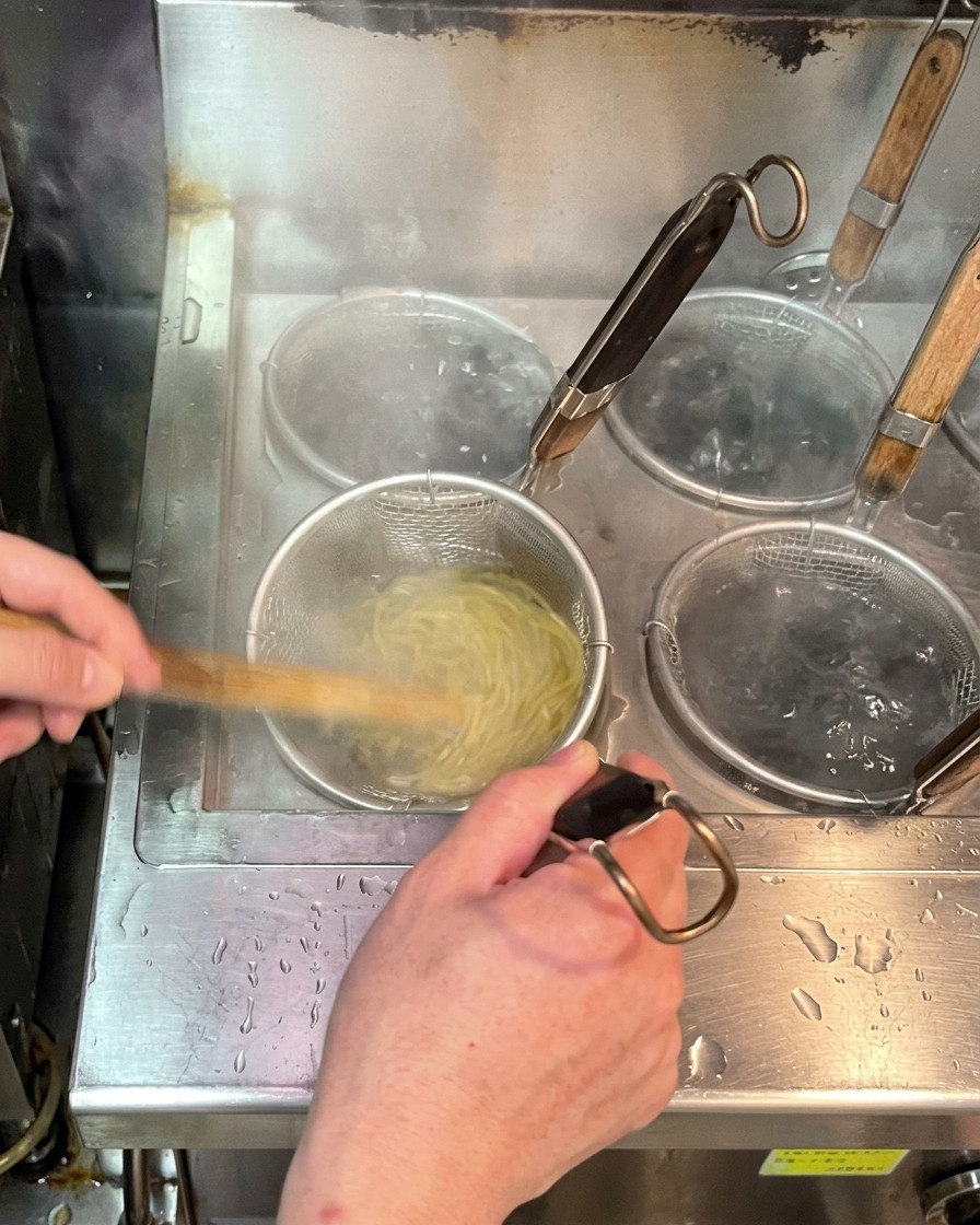 Nouilles ramen fraîches cuisant dans un panier métallique immergé dans une casserole deau bouillante.
