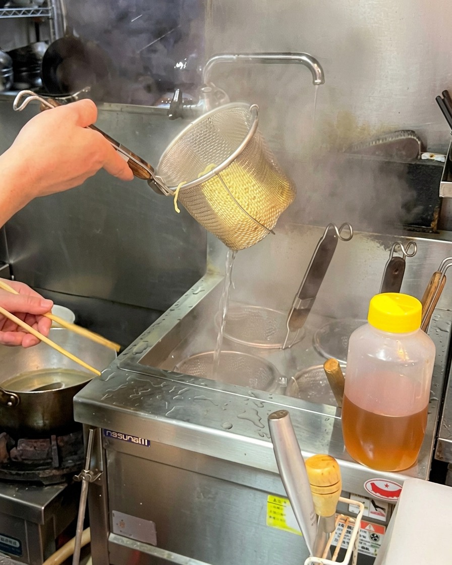 Un chef secouant fermement un panier de nouilles ramen cuites pour en extraire lexcédent deau.