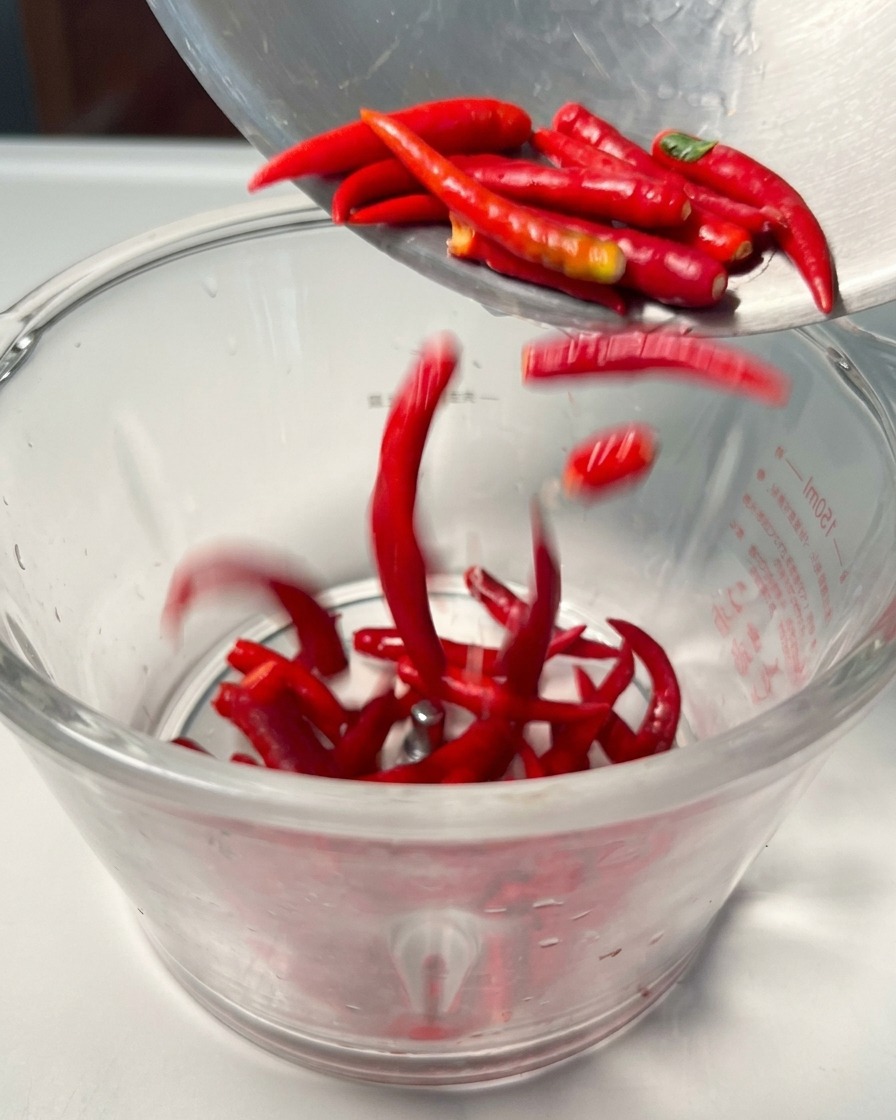 Piments rouges frais versés dans le bol dun robot culinaire.
