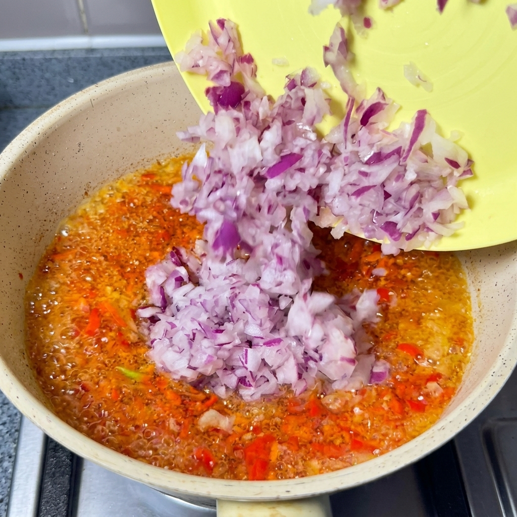 Oignons rouges hachés versés dune assiette jaune dans lhuile de piment frémissante.