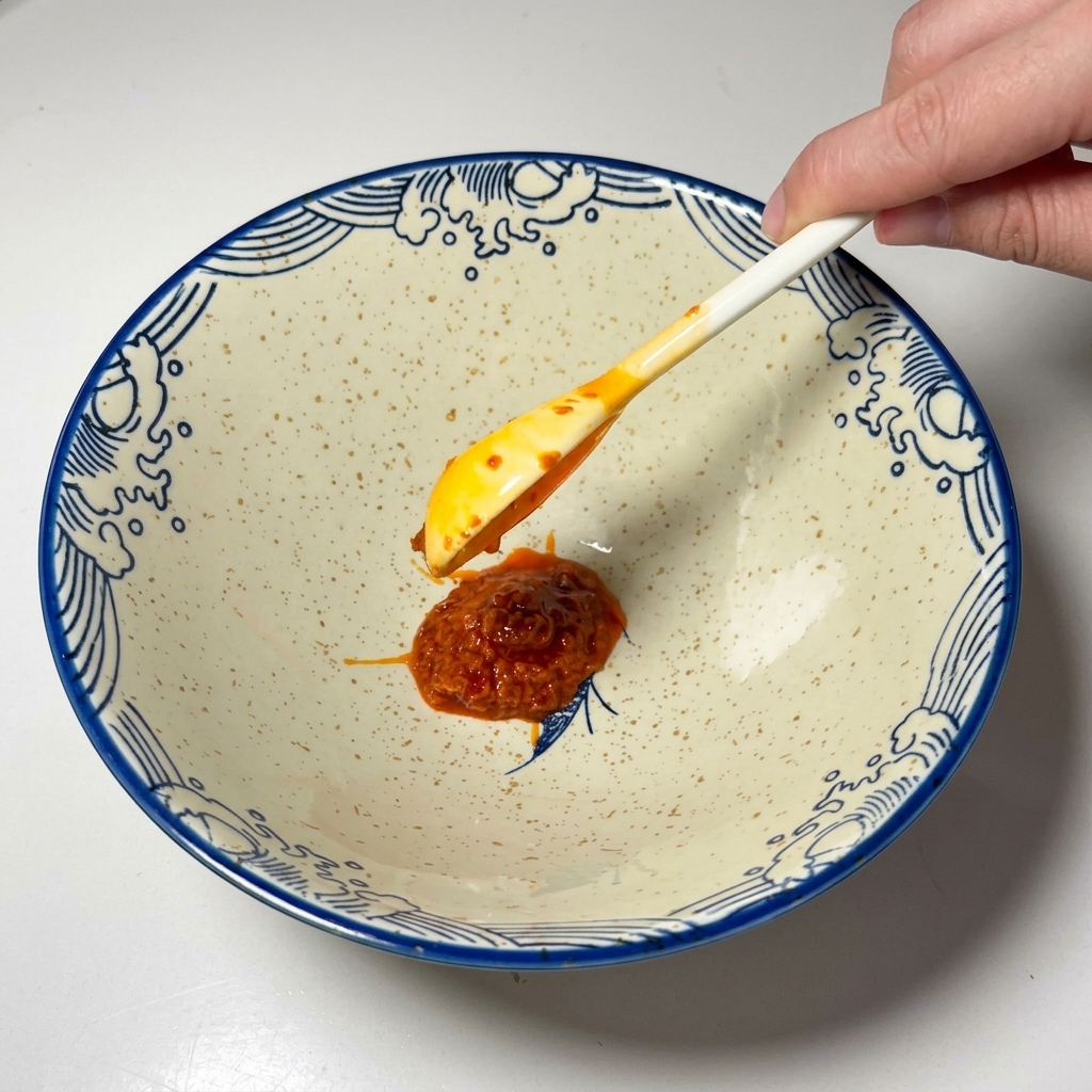 Une cuillerée de pâte de piment rouge vif déposée au fond dun bol en céramique.
