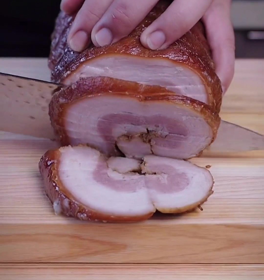 Mains utilisant un couteau tranchant pour découper le chashu froid en rondelles épaisses sur une planche.