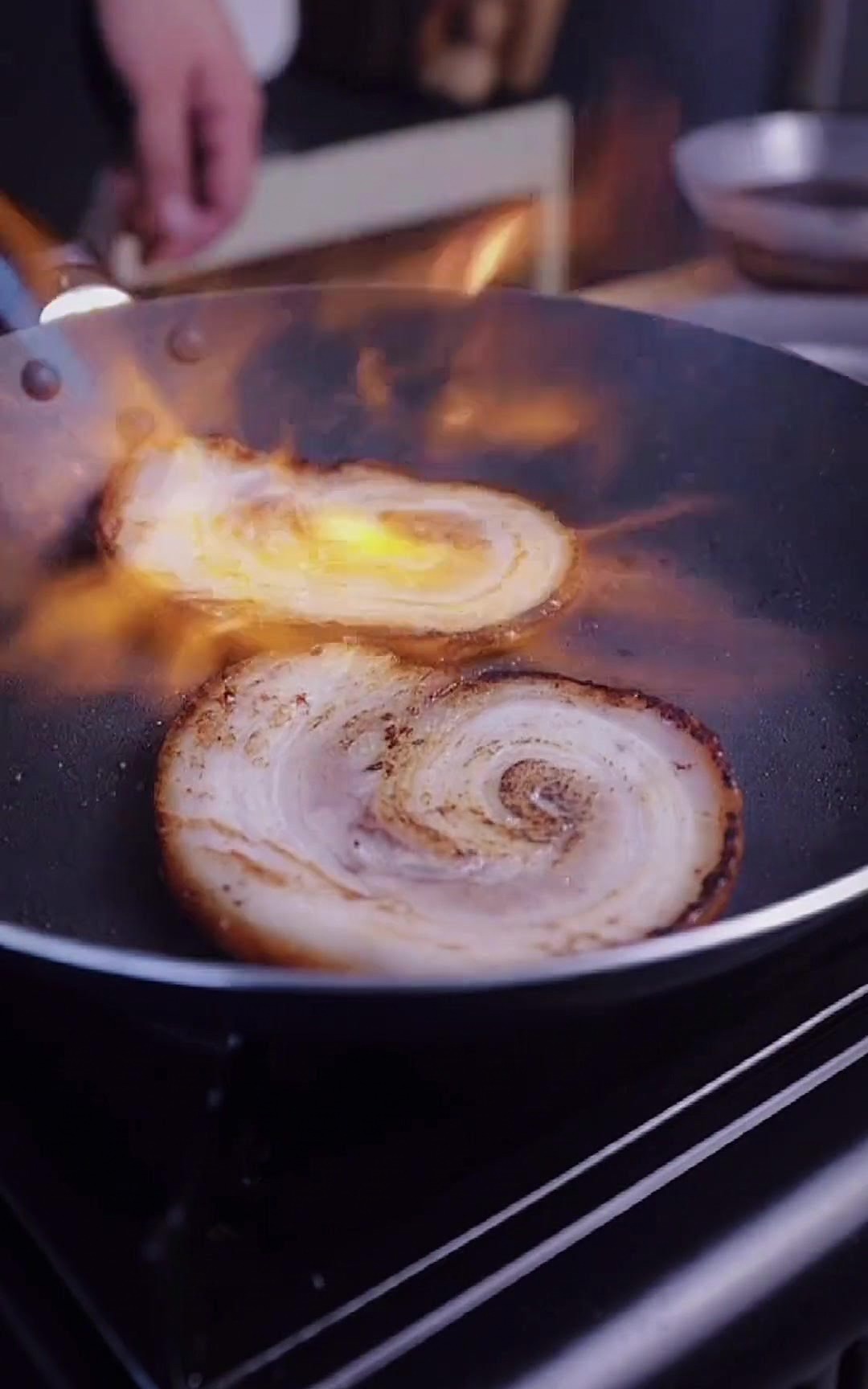Flamme orange dun chalumeau de cuisine percutant une tranche de chashu dans la poêle.