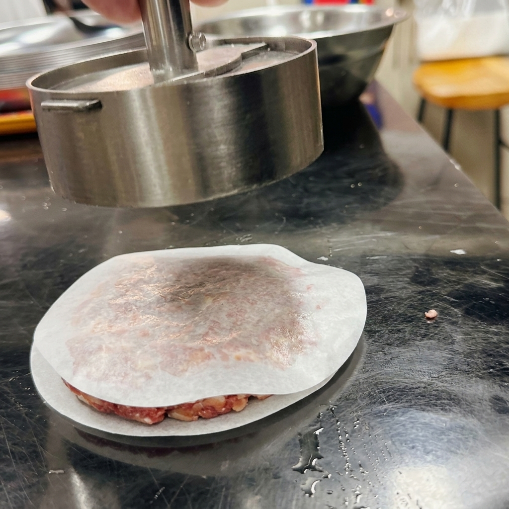 Une presse à burger métallique façonnant le bœuf haché sur une feuille de papier sulfurisé.