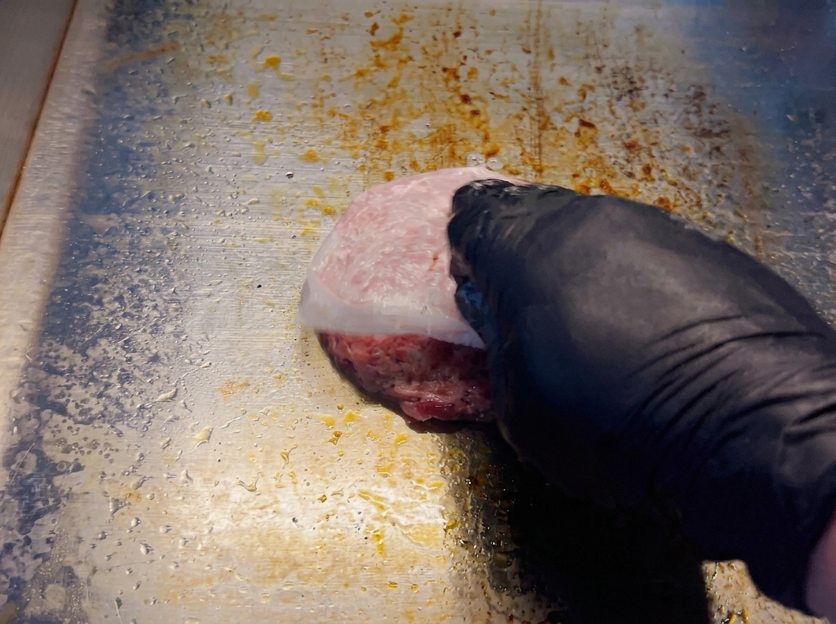 Une main retirant le papier sulfurisé dun steak de bœuf cru sur une plaque de cuisson brûlante.