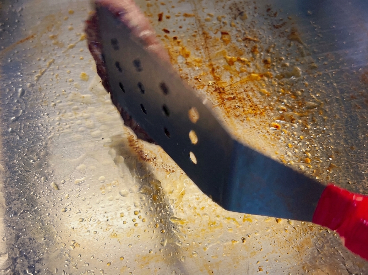 Une spatule métallique retournant un steak de bœuf montrant une belle croûte brune.