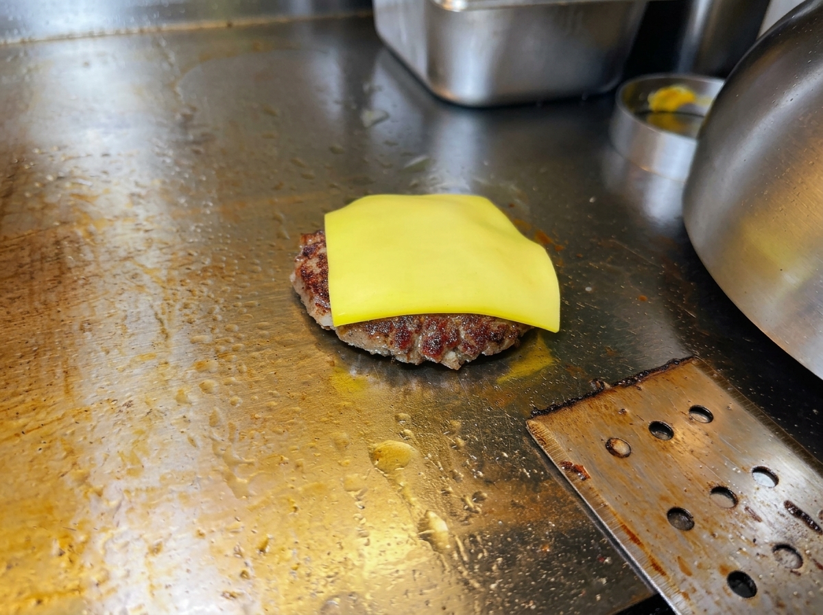 Une tranche de fromage jaune commençant à fondre sur un steak de bœuf grillé.
